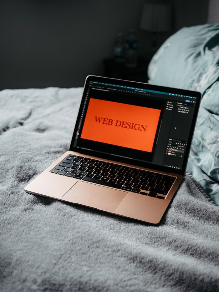 A laptop on a bed displaying web design software, setting up a cozy workspace.